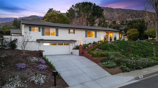 view of front facade with stucco siding, concrete driveway, a mountain view, and an attached garage