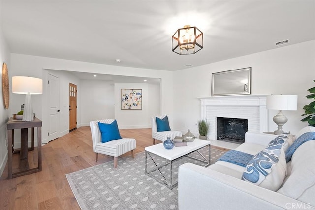 living area featuring wood finished floors, baseboards, a fireplace with flush hearth, and a chandelier