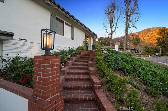 view of side of property with brick siding, stucco siding, a mountain view, and stairs