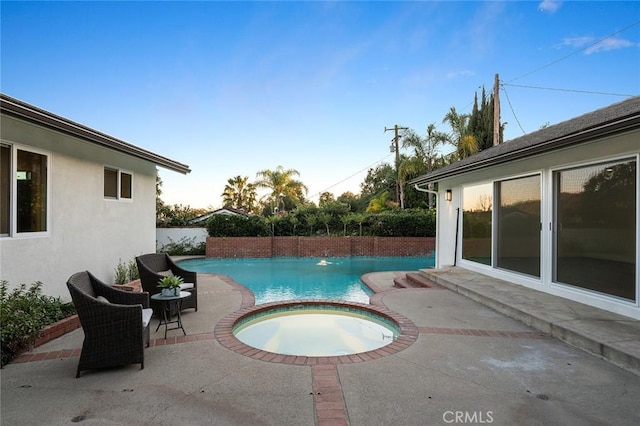 pool at dusk with a patio, a pool with connected hot tub, and fence