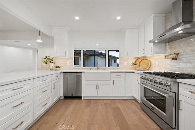 kitchen with wall chimney exhaust hood, stainless steel appliances, a sink, white cabinetry, and light countertops
