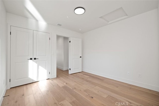 unfurnished bedroom featuring attic access, baseboards, light wood finished floors, and a closet