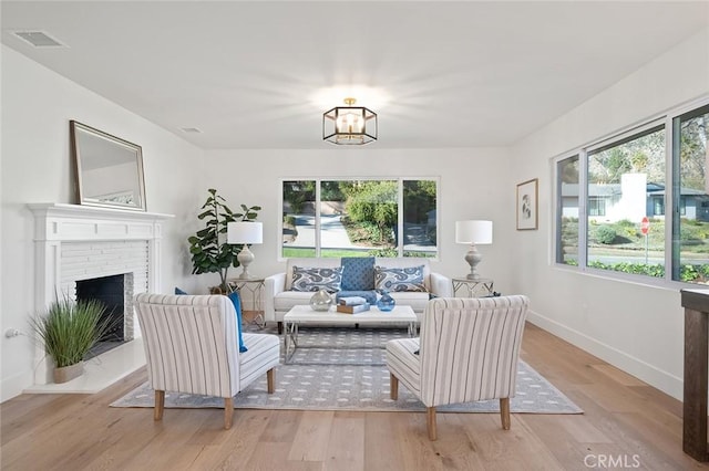 living area featuring light wood finished floors, baseboards, a chandelier, and a brick fireplace