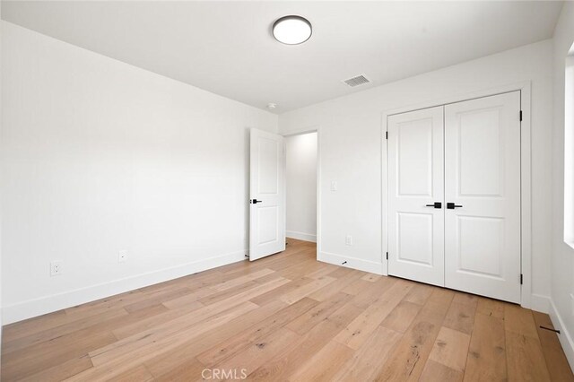unfurnished bedroom with light wood-style flooring, baseboards, and a closet