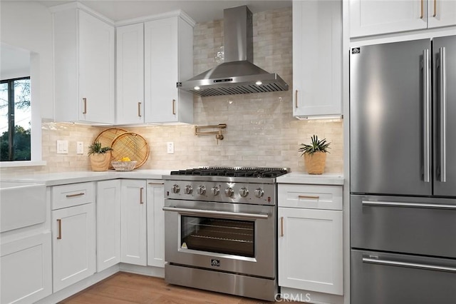 kitchen with high end appliances, wall chimney exhaust hood, light countertops, and white cabinets