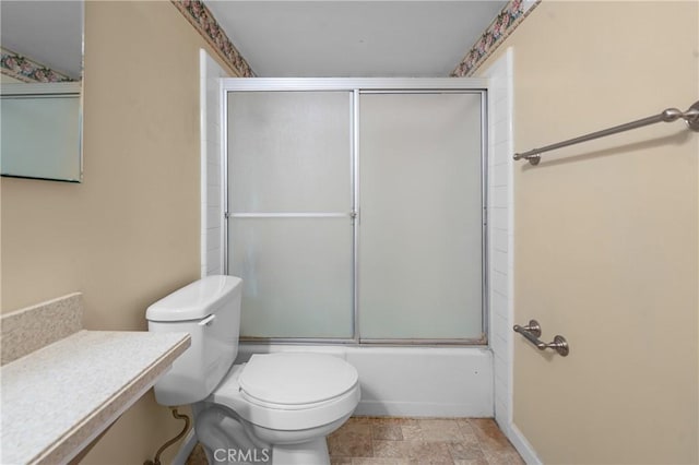 full bathroom featuring stone finish floor, combined bath / shower with glass door, and toilet