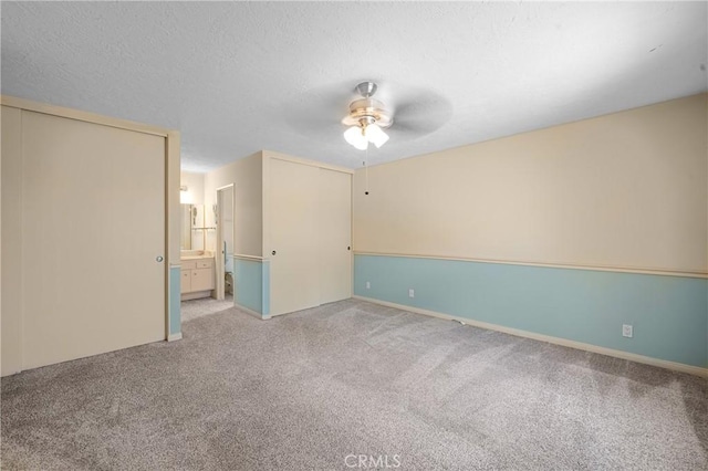 unfurnished bedroom with ensuite bath, ceiling fan, a textured ceiling, and light colored carpet