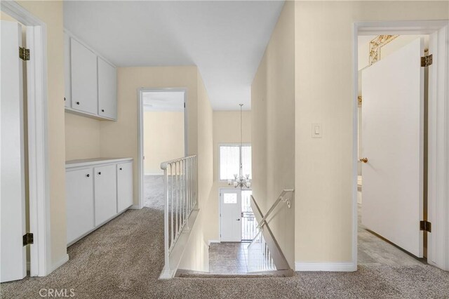 hall with baseboards, a chandelier, and light colored carpet