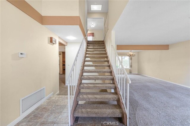 stairway with carpet, visible vents, a chandelier, baseboards, and tile patterned floors