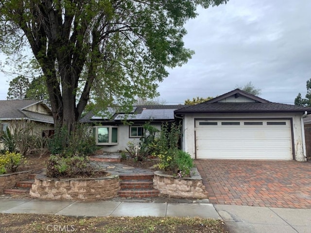 ranch-style home featuring an attached garage, decorative driveway, roof mounted solar panels, and stucco siding