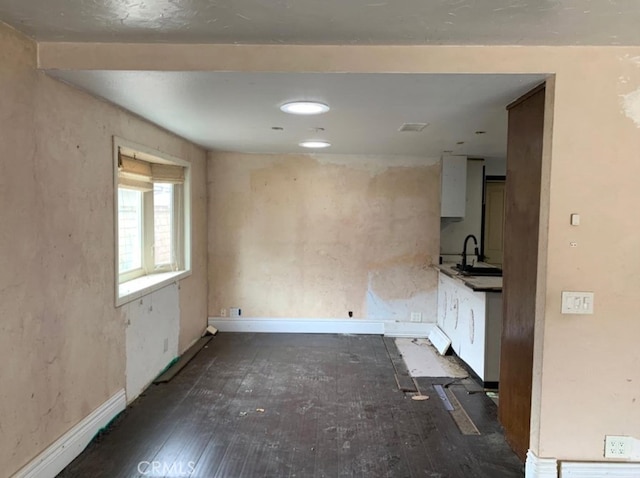 empty room featuring baseboards, wood-type flooring, and a sink