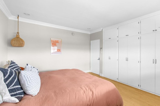 bedroom featuring light wood-style floors, ornamental molding, and multiple closets