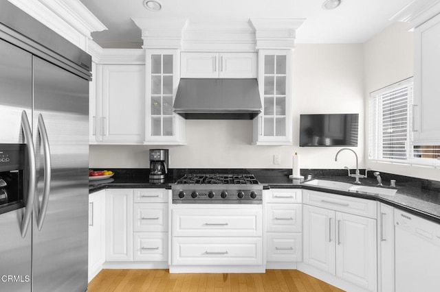 kitchen with light wood-style flooring, appliances with stainless steel finishes, white cabinetry, a sink, and exhaust hood