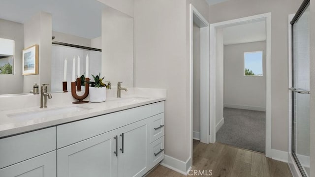 full bathroom with double vanity, a shower with door, a sink, and wood finished floors