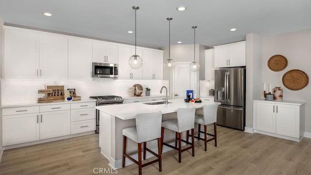 kitchen featuring a breakfast bar, a center island with sink, stainless steel appliances, light wood-style flooring, and a sink