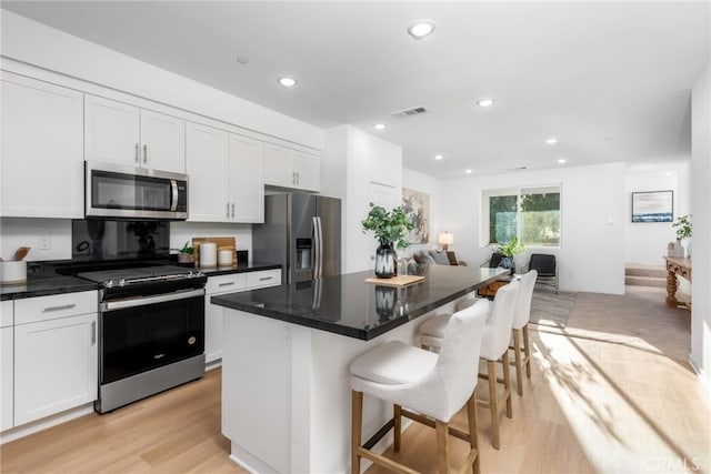 kitchen with white cabinetry, appliances with stainless steel finishes, open floor plan, and a kitchen breakfast bar