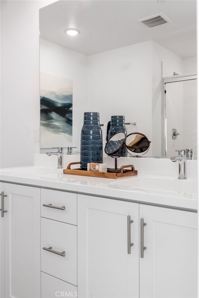 bathroom with double vanity, walk in shower, a sink, and visible vents