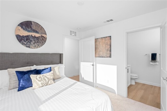 bedroom featuring light wood-style floors, visible vents, baseboards, and ensuite bathroom