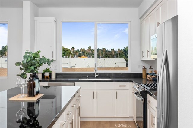 kitchen with appliances with stainless steel finishes, a sink, white cabinetry, and a healthy amount of sunlight