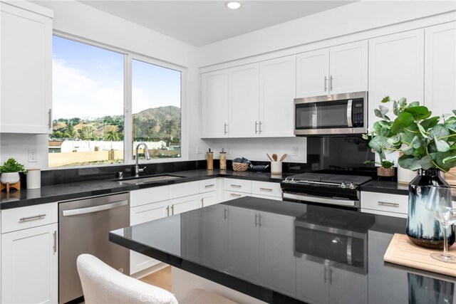 kitchen with recessed lighting, a sink, white cabinetry, appliances with stainless steel finishes, and dark countertops