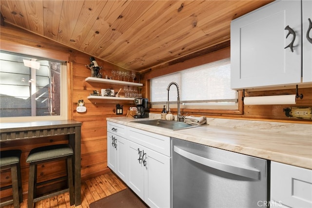 kitchen featuring light wood-style flooring, a sink, light countertops, wood walls, and stainless steel dishwasher
