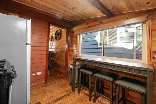 interior space featuring wooden ceiling, wood walls, light wood-style floors, freestanding refrigerator, and gas stove