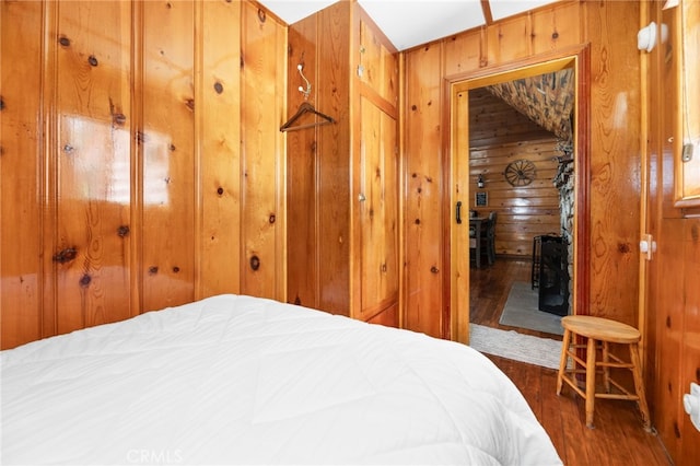 bedroom featuring wood finished floors, wood walls, and a wood stove