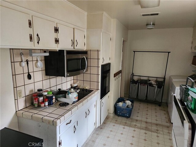 kitchen featuring tile countertops, visible vents, white cabinets, black oven, and stainless steel microwave