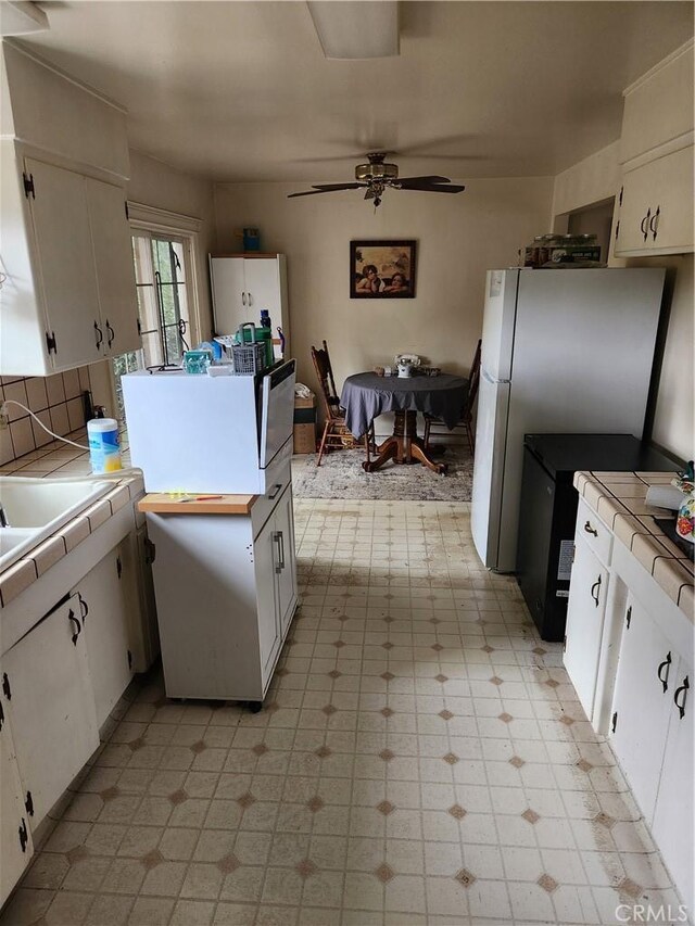 kitchen featuring light floors, freestanding refrigerator, tile counters, and white cabinets