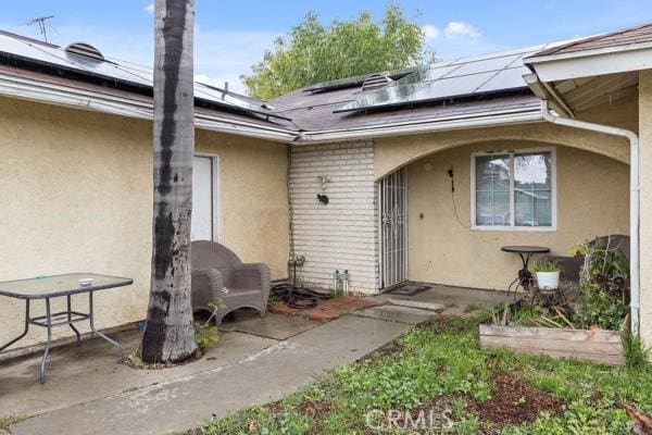 doorway to property with brick siding, a patio area, and stucco siding