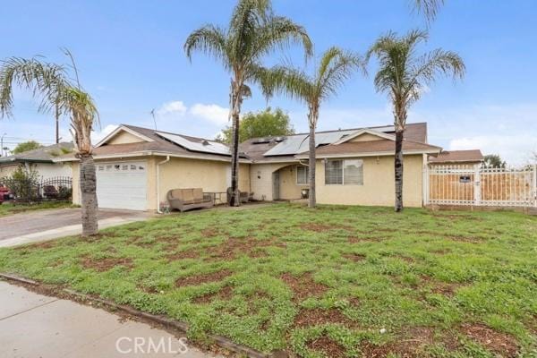 ranch-style home with a front yard, fence, driveway, solar panels, and an attached garage