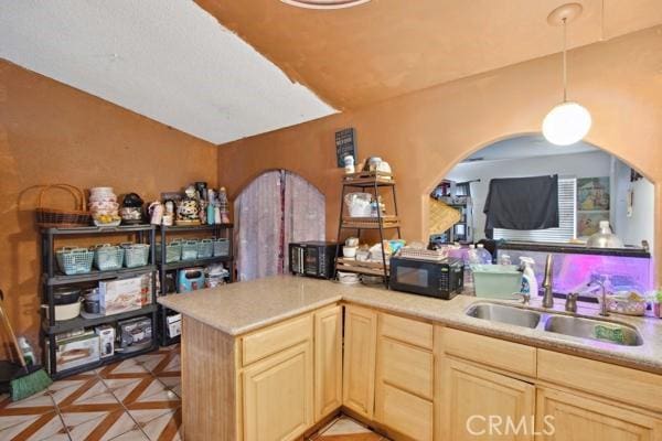 kitchen featuring a sink, black microwave, light brown cabinets, and light countertops