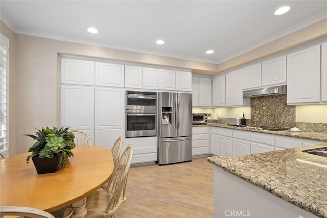 kitchen with under cabinet range hood, white cabinetry, light wood-style floors, ornamental molding, and appliances with stainless steel finishes