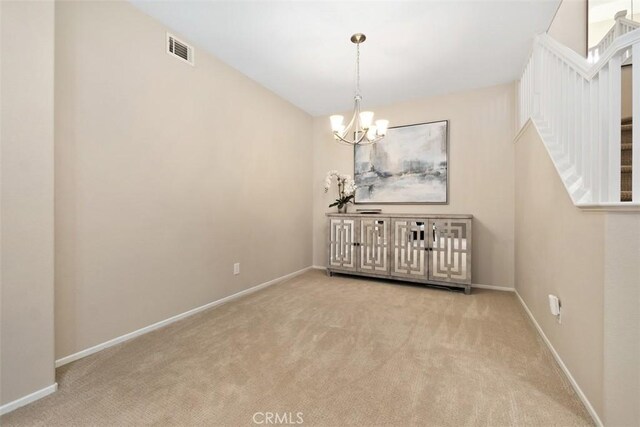 spare room with a chandelier, carpet flooring, visible vents, baseboards, and stairway