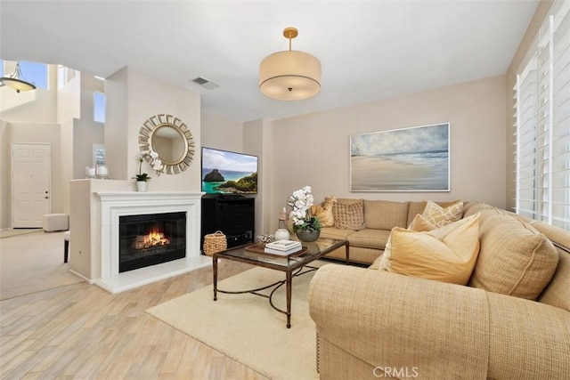 living area with a glass covered fireplace, wood finished floors, visible vents, and a healthy amount of sunlight