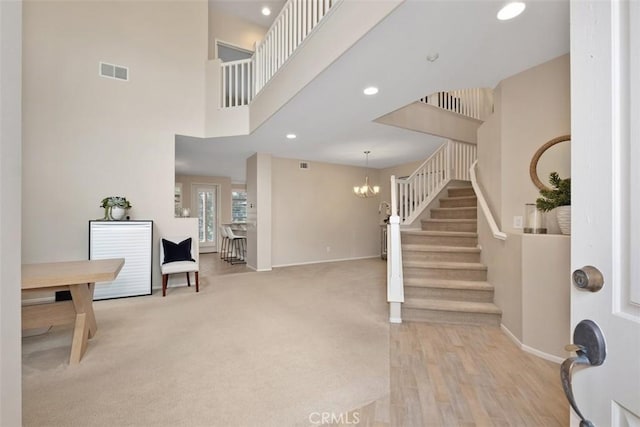 entryway with baseboards, visible vents, a towering ceiling, stairway, and an inviting chandelier