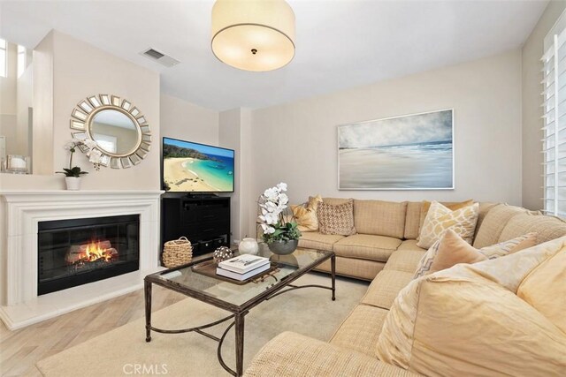 living room featuring wood finished floors, a glass covered fireplace, and visible vents