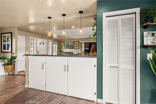 kitchen featuring decorative light fixtures, dark countertops, wood finished floors, a peninsula, and white cabinets