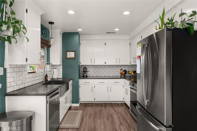 kitchen with dark countertops, dark wood finished floors, appliances with stainless steel finishes, white cabinets, and a sink