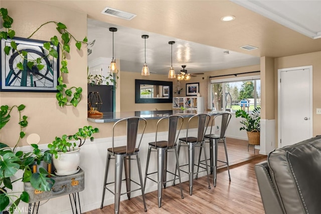 kitchen featuring visible vents, a kitchen bar, a peninsula, and wood finished floors