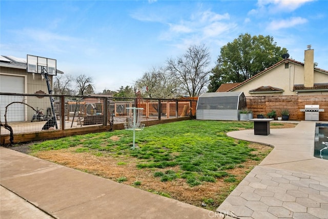 view of yard with a shed, a patio area, a fenced backyard, an outbuilding, and a vegetable garden