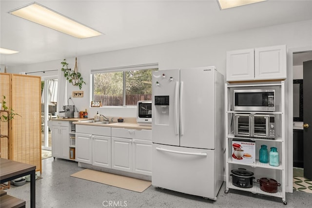 kitchen featuring stainless steel microwave, light countertops, white refrigerator with ice dispenser, white cabinets, and a sink