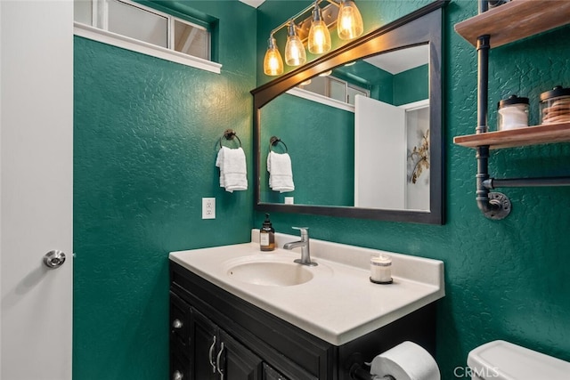 bathroom with toilet, vanity, and a textured wall