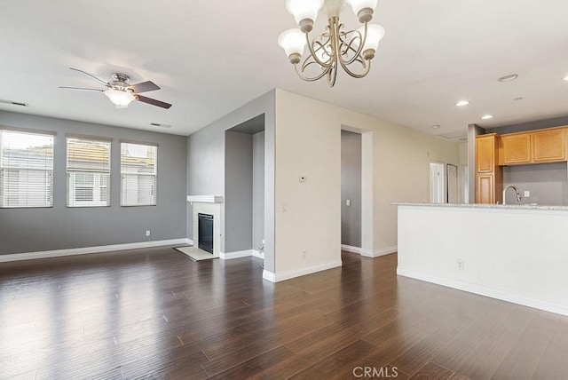 unfurnished living room featuring dark wood finished floors, a tiled fireplace, a sink, baseboards, and ceiling fan with notable chandelier