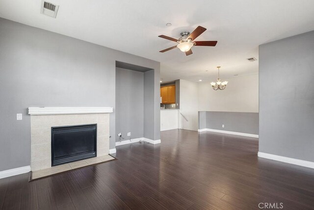 unfurnished living room featuring ceiling fan with notable chandelier, a fireplace, wood finished floors, visible vents, and baseboards