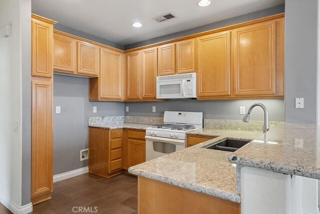 kitchen featuring white appliances, visible vents, a peninsula, light stone countertops, and a sink