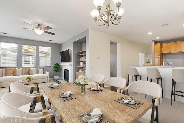 dining space with recessed lighting, ceiling fan with notable chandelier, a fireplace with flush hearth, visible vents, and light wood-type flooring