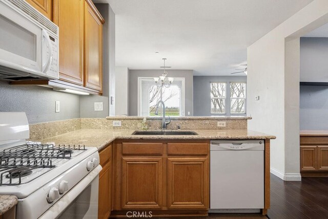 kitchen with dark wood-style flooring, a sink, light stone countertops, white appliances, and a peninsula