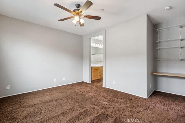 unfurnished bedroom featuring dark colored carpet, ceiling fan, baseboards, and ensuite bathroom