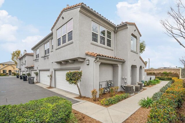 view of side of property with a garage, a tiled roof, central AC unit, and stucco siding